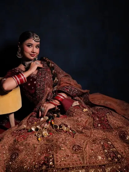 A seated portrait showcasing the beautiful flare of this maroon bridal lehenga. The choker, earrings, and maang tikka are all part of the rental set I provide.