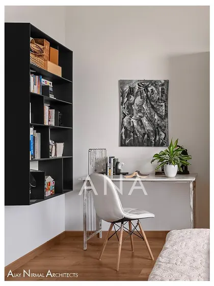 The study corner in a guest bedroom of Apartment 704. A wall-mounted bookshelf and a simple desk create a functional workspace without cluttering the room.