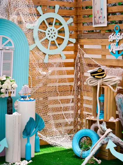 "Let's Get Nauti" with this fun nautical theme. Featuring a ship's wheel, fishing nets, and an anchor, this setup is great for birthdays, bachelorettes, or even a unique proposal.