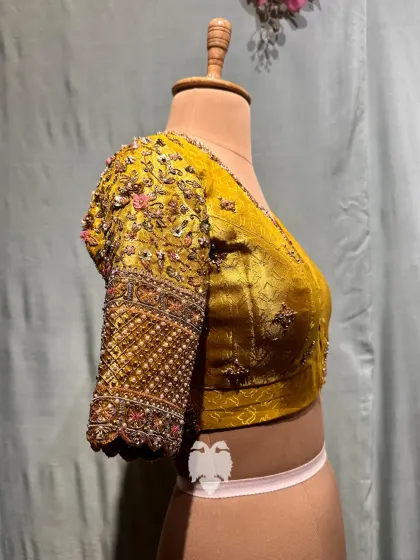 A side view of a yellow tissue blouse, showing the delicate creeper motifs on the sleeves touched with pink and green sparkle.