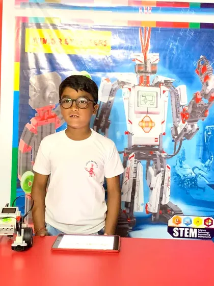 A student proudly stands with his programmed robot, built using a LEGO WeDo 2.0 kit, ready to demonstrate its capabilities.