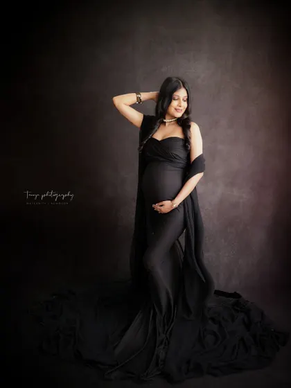 A dramatic and stylish portrait against a dark, moody background. The mom-to-be's black gown and confident pose create a powerful and glamorous image.