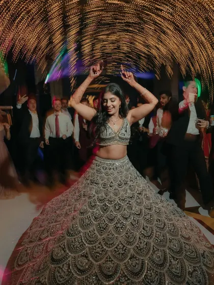 A moment of pure joy on the dance floor. The bride's wide smile and twirling lehenga, surrounded by motion-blurred lights, perfectly capture the energy and happiness of the reception.