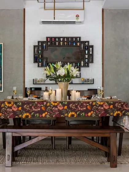 This dining space blends contemporary minimalism with rustic charm. A solid wood bench is paired with upholstered chairs around a table set with a vibrant floral cloth, all against a backdrop of textured grey walls and modern art.