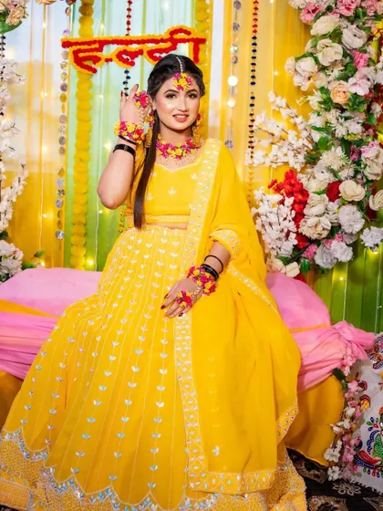 The bride posing for a photo at her Haldi ceremony. The decor, with its floral arch and bright yellow theme, creates a picture-perfect moment.