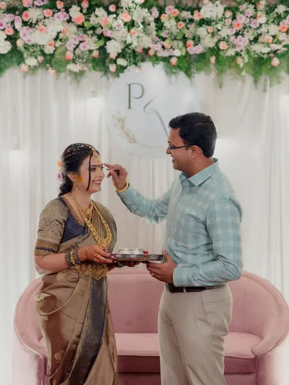 A beautiful moment from an engagement ceremony, with the groom placing a tilak on the bride's forehead. The soft pastel decor provides a gentle and romantic setting.