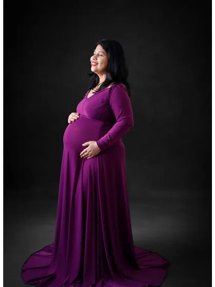 A simple and elegant portrait in a full-length purple gown. The solid dark background keeps the focus on the beautiful color and silhouette.