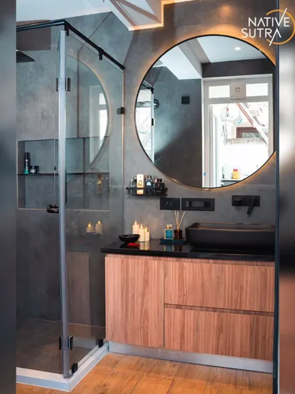 A detailed view of the vanity area, with a wooden cabinet providing warmth against the cool concrete-finish tiles. The backlighting on the mirror adds a dramatic and luxurious touch.