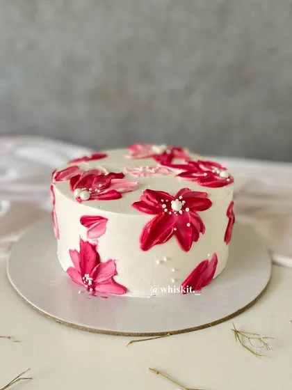 A flat cake decorated with abstract palette knife flowers in a vibrant magenta. The scattered edible pearls add a touch of delicate detail.