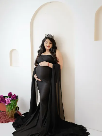 A regal and elegant portrait. The mom-to-be wears a crown and a flowing black gown, her pose full of grace and confidence.