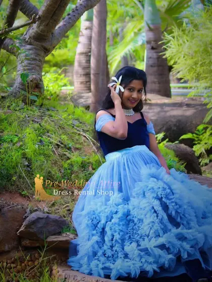 This unique gown features a dark blue velvet top with an off-shoulder neckline and a voluminous, ruffled sky-blue skirt. It combines texture and color for a high-fashion look.
