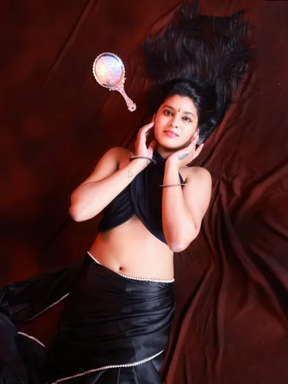 An artistic flat-lay style portrait. The model's hair is fanned out, and the placement of the hand mirror adds a creative element to this studio shot of a modern black saree.