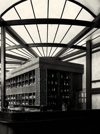 The corner of the bar, showing the detailed fretwork panel and the extensive bottle display. The design combines functionality with decorative, art-deco inspired elements.