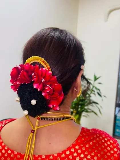 A voluminous hair bun for the mother of the bride, decorated with red flowers and pearls. This is a classic look for Maharashtrian weddings.