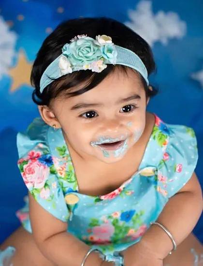 A sweet, frosting-covered smile after a fun cake smash. The starry blue background adds a touch of magic to her first birthday photos.