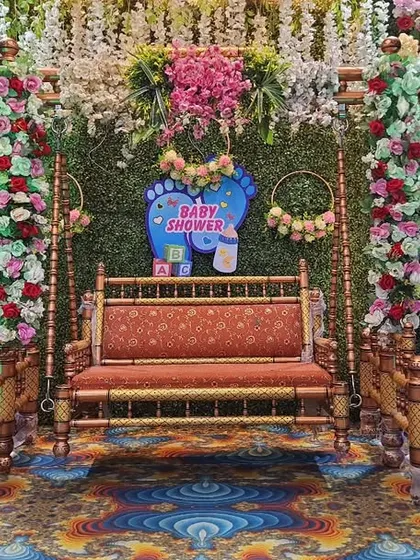 This gender reveal decoration features a lush green backdrop that makes the floral colors pop. The setup includes a central swing, Radha-Krishna cutouts, and 'It's a Boy/Girl' signs, perfect for a vibrant Dohale Jevan.