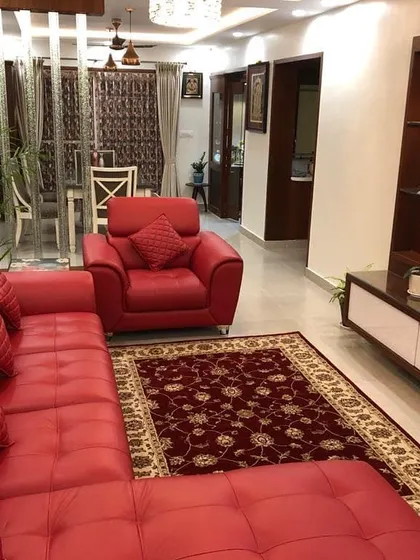 A vibrant living room designed for comfort, featuring a plush, quilted red leather sectional sofa. A simple white media unit sits opposite, and the space is defined by a traditional red patterned rug, creating a cozy and inviting atmosphere.
