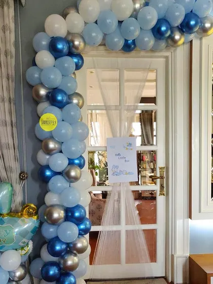 A simple and elegant door entrance decoration for a baby boy's welcome. The blue and silver balloon arch and a small welcome sign create a lovely greeting for the new arrival.