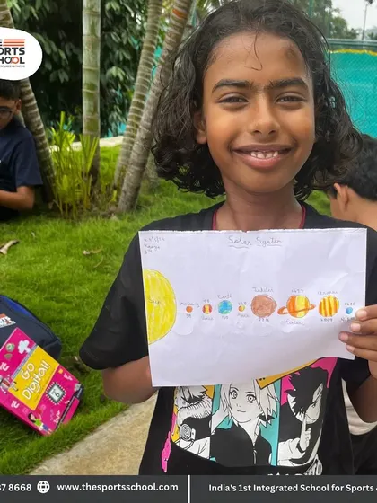 A smiling student displays her colorful drawing of the solar system.