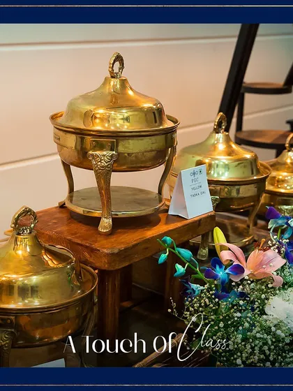 A close-up of an ornate brass chafing dish. The text overlay "A touch of Class" aptly describes how our choice of serveware adds a layer of sophistication to the dining experience.