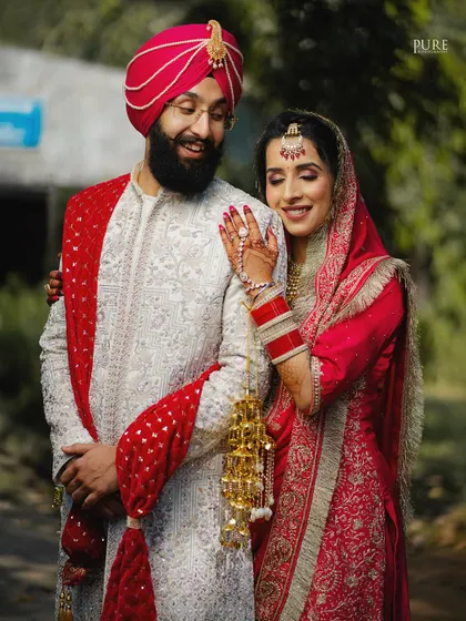 A classic portrait of a Sikh couple. The bride's hand on her groom's shoulder and their happy expressions showcase their connection and the beauty of their traditional attire.