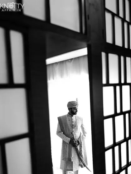 A powerful black and white portrait of the groom holding a ceremonial sword, framed by a doorway. This shot is full of tradition and strength.