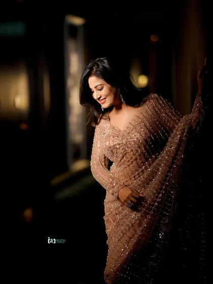 This shot captures a candid, in-between moment. The dark, moody lighting creates a cinematic feel, focusing on the silhouette and the sparkle of the saree.