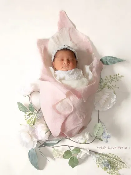A little flower ready to bloom. This artistic shot shows a newborn wrapped in white, nestled inside a large, soft pink fabric flower, symbolizing new life.