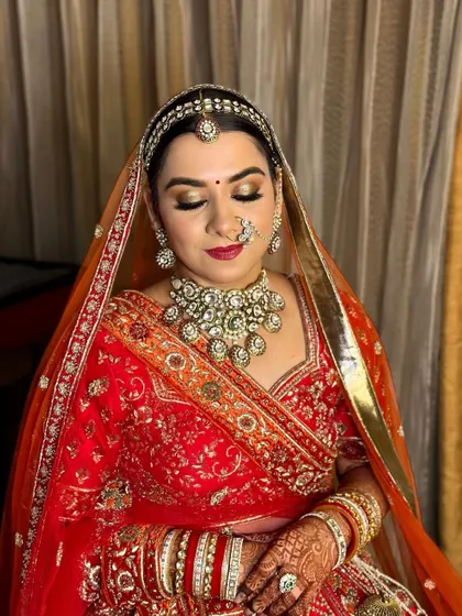 A classic red bride with a double dupatta. The makeup features golden eyes and a deep red lip, perfectly complementing her ornate jewelry and attire.