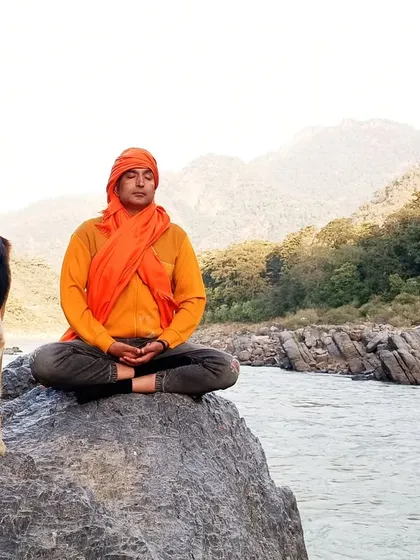 A moment of profound peace. Our Yogacharya meditates on a rock by the Ganges, embodying the stillness we teach our students to cultivate.