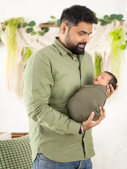 A dad gently holds his sleeping newborn, wrapped snugly in green. This portrait was taken in our boho setup, surrounded by natural textures and plants.