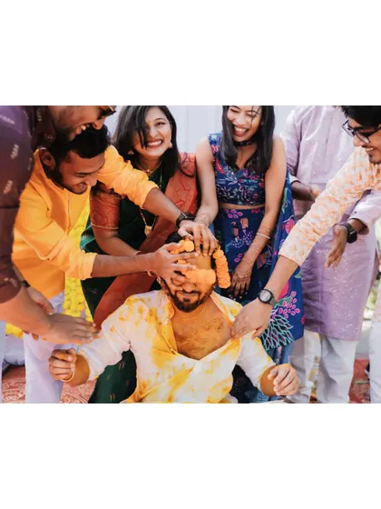 A close-up of the groom surrounded by friends and family, all joining in to apply haldi.