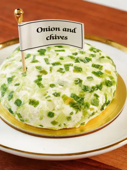 A hero shot of the onion and chives cheese spread, presented like a mini-cake with a flag, making it look special and artisanal.