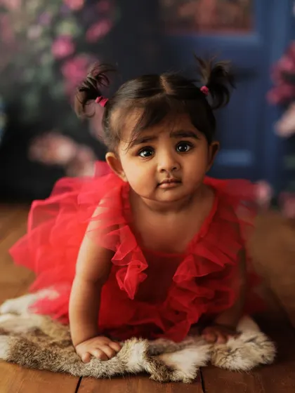 A close-up of a baby girl in a red tutu with cute pigtails. This shot captures her doll-like features and innocent expression.