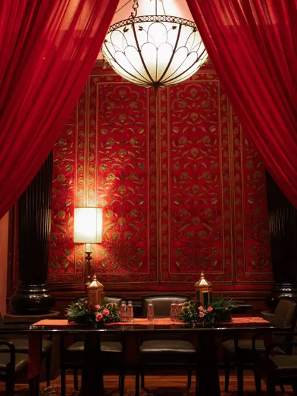 An intimate and regal dining setup for a royal-themed engagement, featuring a rich red backdrop and ornate traditional lamps.