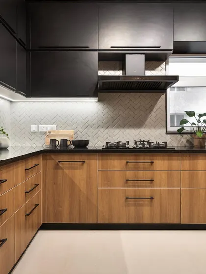 The two-tone kitchen from the 'Ikigai Living' project combines wood-grain lower cabinets with sleek black upper units. A herringbone tile backsplash adds a touch of classic pattern to this modern and functional kitchen design.
