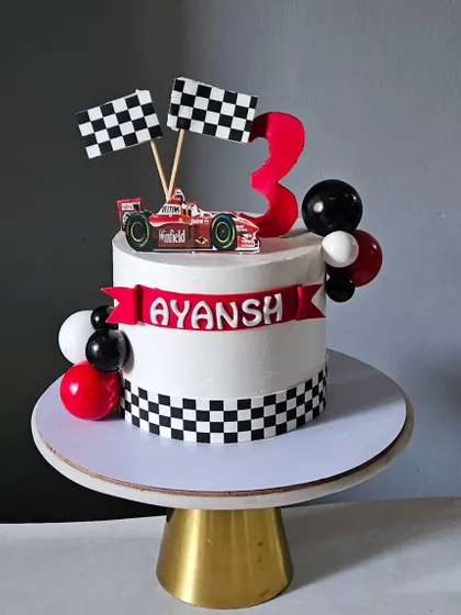 Ready, set, celebrate! A race car theme cake perfect for a little racer's third birthday, complete with checkered flags, a Ferrari car topper, and a personalized name banner.