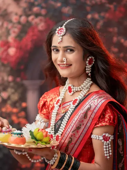 A vibrant portrait of a woman holding a thali during her festive photoshoot. The warm, glowing background and her joyful expression perfectly capture the celebratory atmosphere.