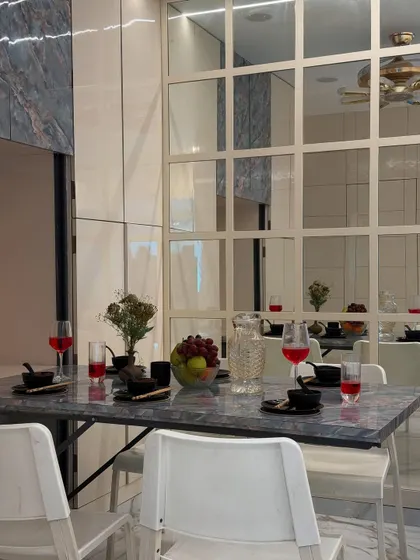 A detailed shot of the dining setup, showing the elegant marble-patterned tabletop against the gridded mirror wall. These details create a feeling of luxury and openness.