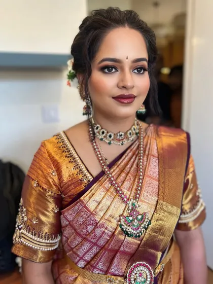 A classic South Indian bridal look with a beautiful gold and maroon saree. The eye makeup is a soft smokey brown with a touch of shimmer, paired with a bold lip for a timeless feel.