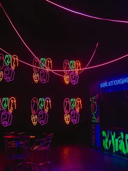 A view of the party space showing the neon signs and a graffiti art bar. We used UV paint and blacklights to make the artwork glow, adding to the underground club feel.