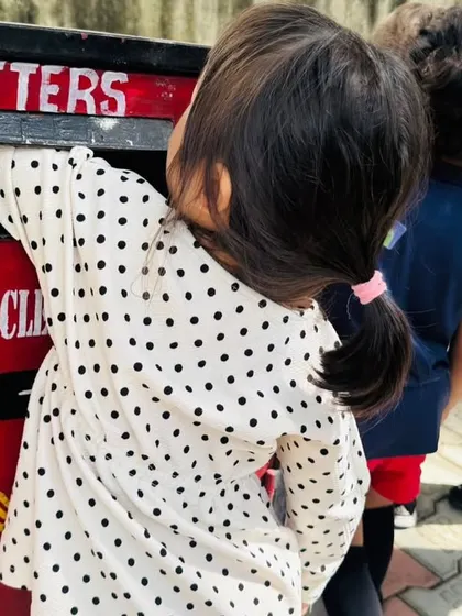 A child carefully posts a letter she wrote to her parents into the bright red postbox.