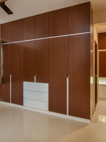 A large, floor-to-ceiling wardrobe in a rich wood laminate, combined with white drawers for a modern contrast. This design provides immense storage capacity for a clutter-free bedroom.