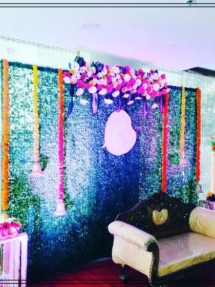 A simple yet elegant baby shower decoration featuring a green grass wall backdrop, floral hangings, and a comfortable sofa for the mother-to-be. This setup is perfect for intimate home functions.