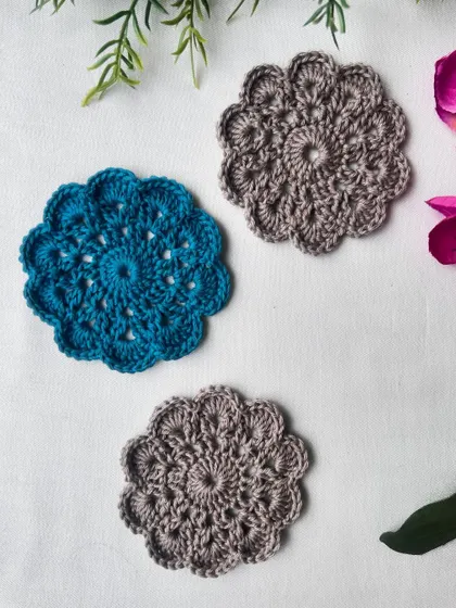 A flat lay of the teal and taupe mandala coaster set, highlighting the intricate stitch work and scalloped edges.
