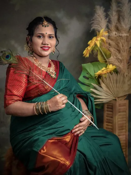 A moment of quiet joy. This mother-to-be, dressed in a lovely green and red saree, holds a peacock feather, a symbol of grace, during her studio maternity session.