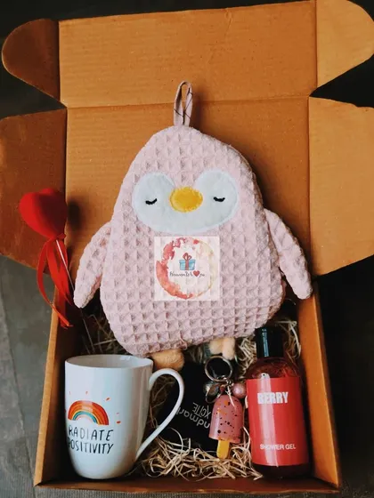 A cozy and positive gift box featuring a "Radiate Positivity" mug, a soft penguin hot water bag, and berry-scented shower oil. A perfect pick-me-up gift.