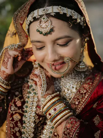 A close-up capturing the bride's gentle smile and the intricate details of her nath (nose ring) and maang tikka. These shots celebrate the fine artistry of bridal adornment.