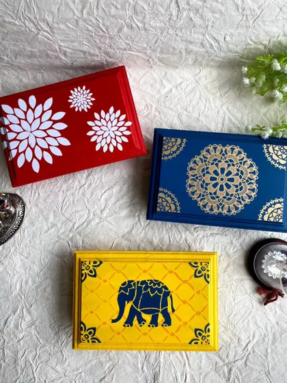 A top-down view of the three pooja chowki designs: red floral, blue mandala, and yellow elephant.