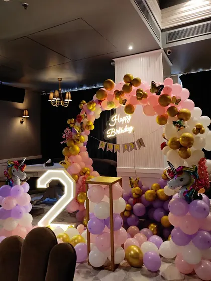 A magical unicorn-themed second birthday party. The setup includes a pink and purple balloon arch, unicorn balloon pillars, a neon sign, and a light-up number '2'.